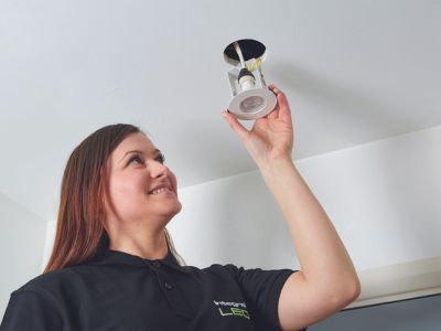 Smiling woman wearing a black Integral LED branded polo shirt installing an evofire firerated downlight into a ceiling
